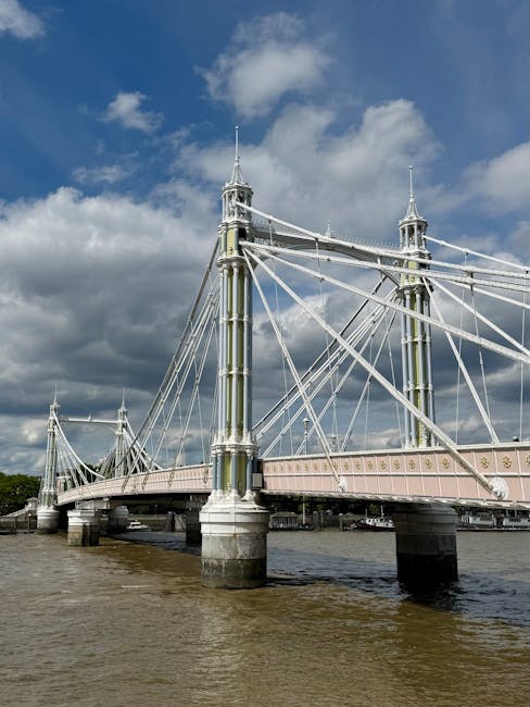 A close-up view of a black metal sign mounted on a stone wall, displaying the emblem of the City of London and reading 'TOWER BRIDGE'. The sign has a slightly arched top with embossed lettering and is